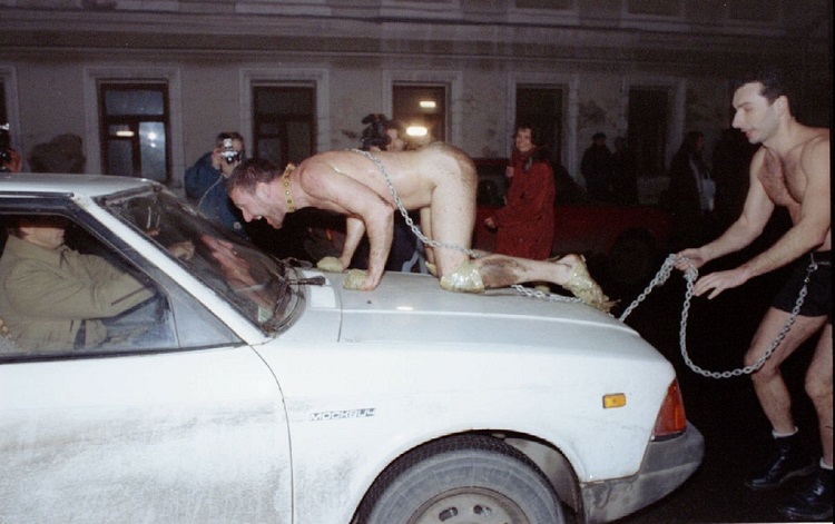 Russian artist Oleg Kulik imitating a dog, jumps on the car of a scared Muscovite as his colleague A..